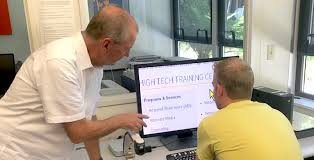 A man is talking with a person who is sitting in front of a computer.