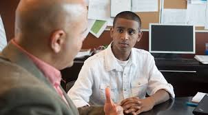 A man is sitting down in an office talking to a student sitting in front of him.