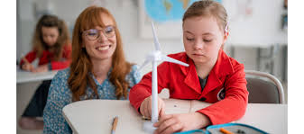 A woman is sitting next to a young girl in a classroom who is holding a model of a wind turbine.